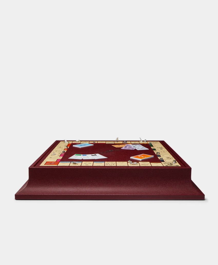 A luxurious Monopoly board game with a deep red base, gold tokens, and classic property cards, viewed from a low front angle against a plain white background.