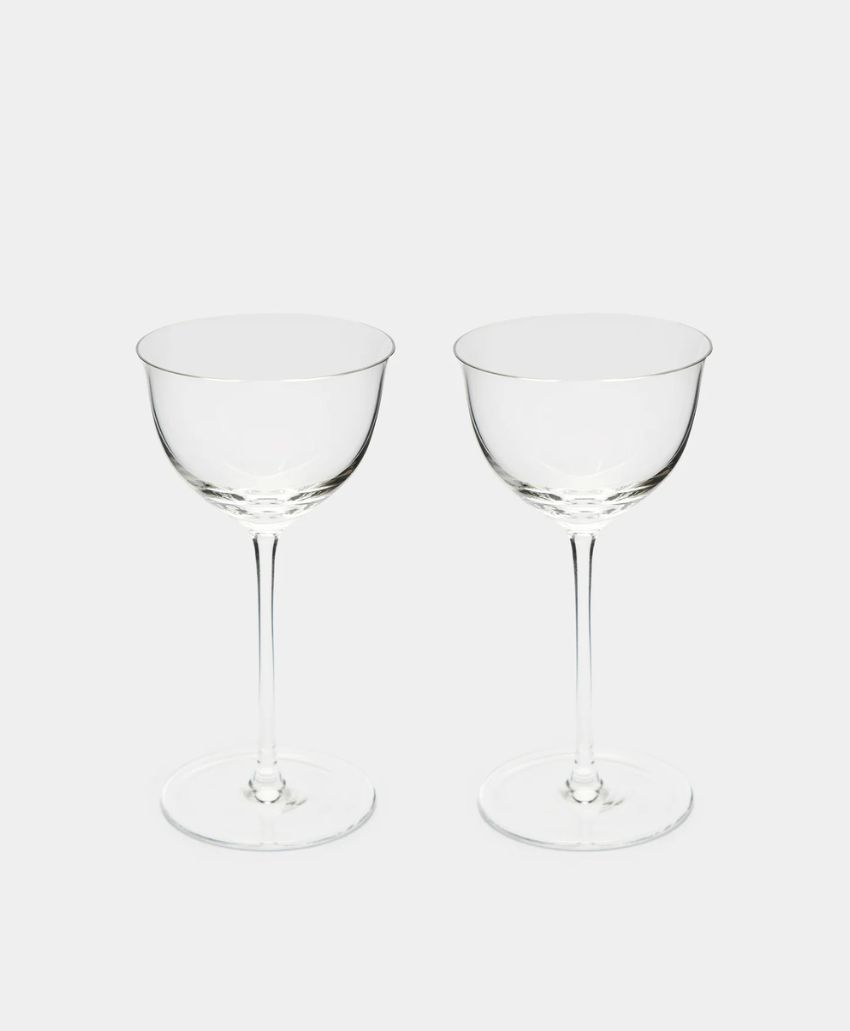 Two clear, empty coupe glasses with long stems are placed side by side on a plain white background.