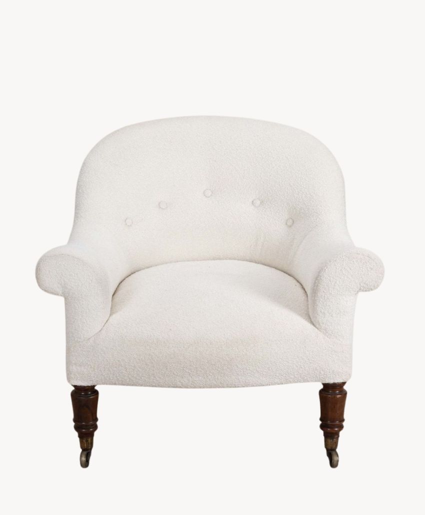 White upholstered armchair with a curved back, three button details, rounded arms, and dark wooden legs with castor wheels on the front two legs. The chair is set against a plain white background.