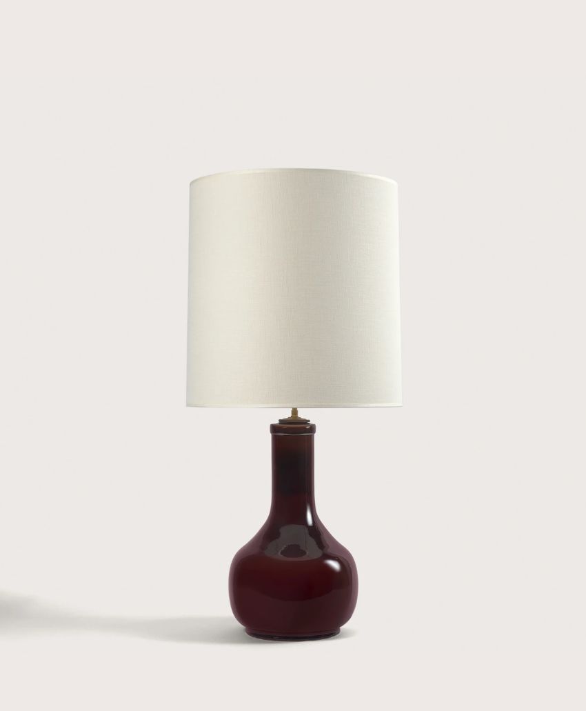 A table lamp with a glossy, dark burgundy ceramic base and a large, cylindrical white lampshade, set against a plain light background.