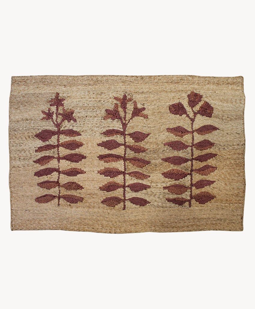 A rectangular woven rug with a natural tan background, featuring three vertical rows of red leafy plant motifs evenly spaced across the surface.