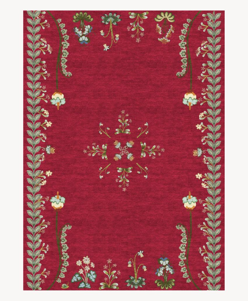 A red rectangular rug with a floral border and small decorative flowers in green, white, blue, and yellow, arranged along the edges and in a central symmetrical pattern.