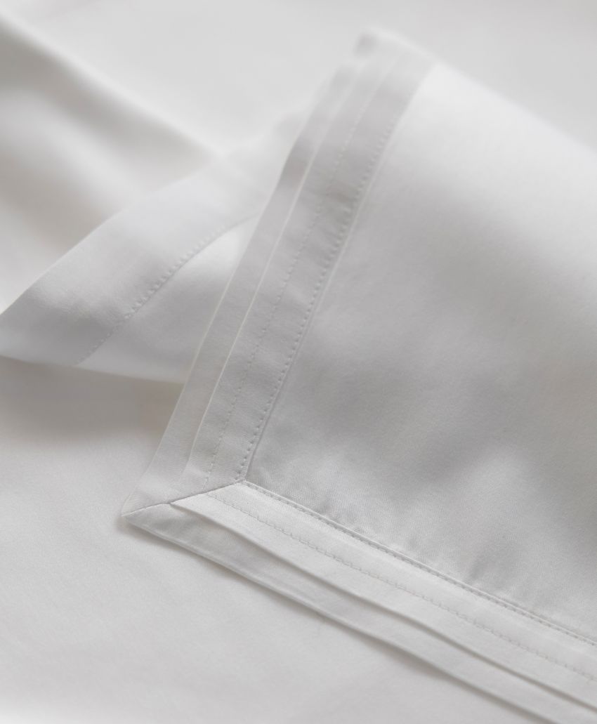 Close-up of crisp, white bed sheets with a smooth texture and neatly stitched edges, highlighting the fabrics quality and clean finish.