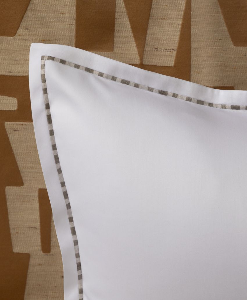 A close-up of a white pillow with a gray and white checked trim, set against a textured brown and beige background with a geometric pattern.