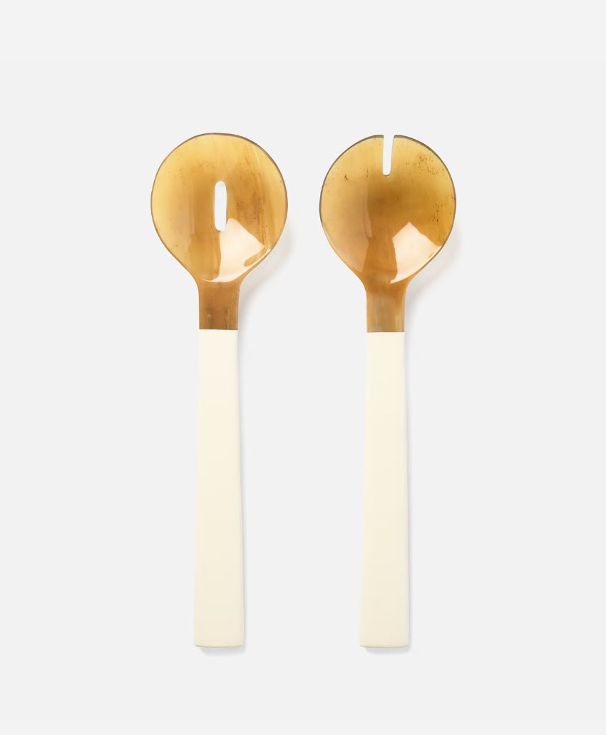 Two salad servers with round, amber-colored heads—one with a slot and one solid—attached to long, ivory handles, placed side by side on a light background.
