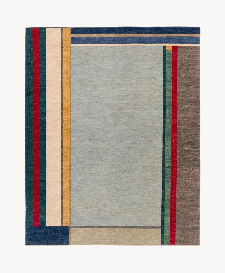 A square area rug with a minimalist geometric design, featuring rectangles and stripes in shades of blue, grey, tan, cream, red, and green on a light grey background.