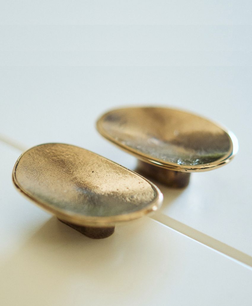 Two oval-shaped, gold-colored cabinet knobs with a textured surface are mounted on a white surface.