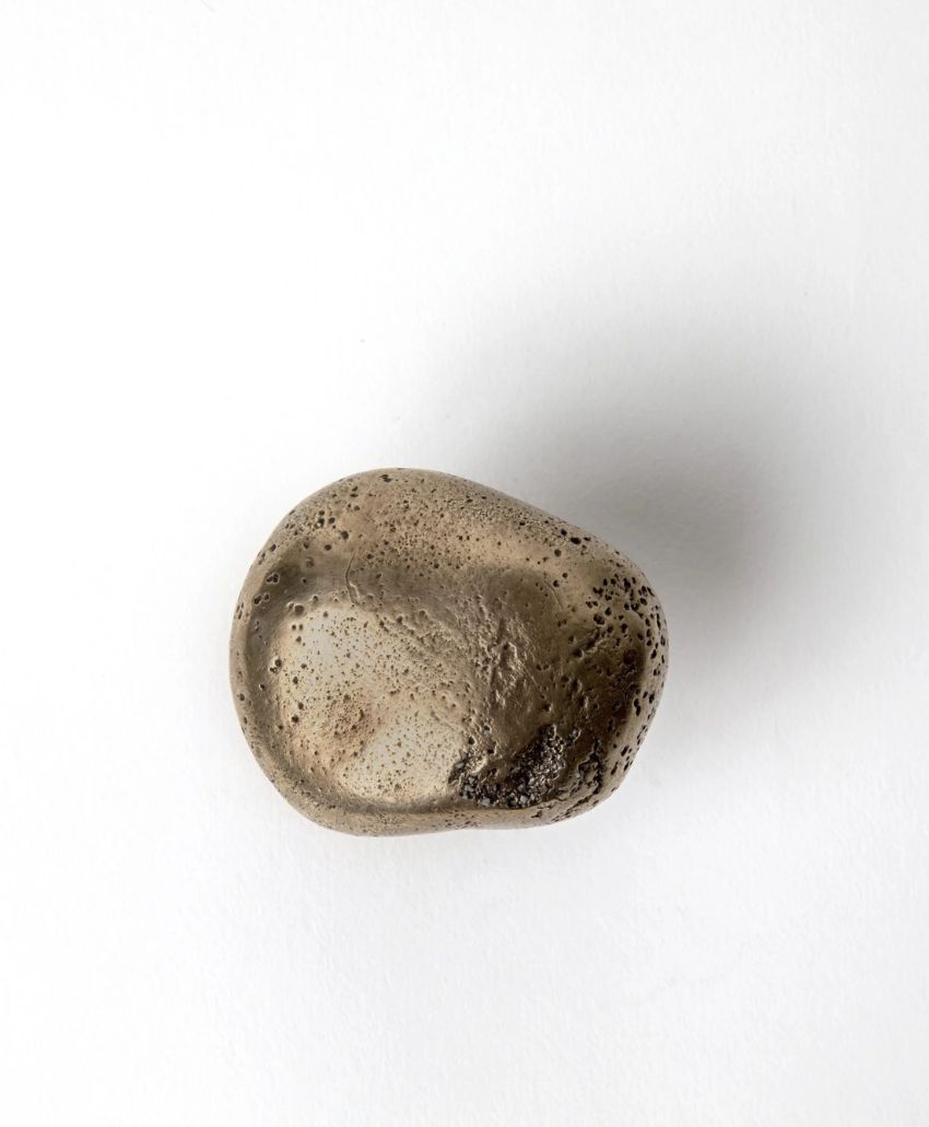 A smooth, oval-shaped stone with a rough, cratered surface and a mix of light brown and dark brown tones, set against a plain white background.