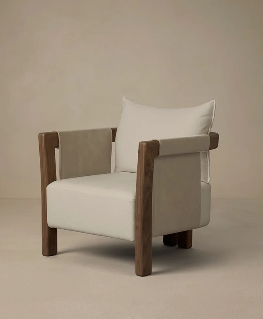 A modern armchair with light beige upholstery and sturdy wooden frame, featuring thick, square armrests and a plush back cushion, set against a plain, neutral background.