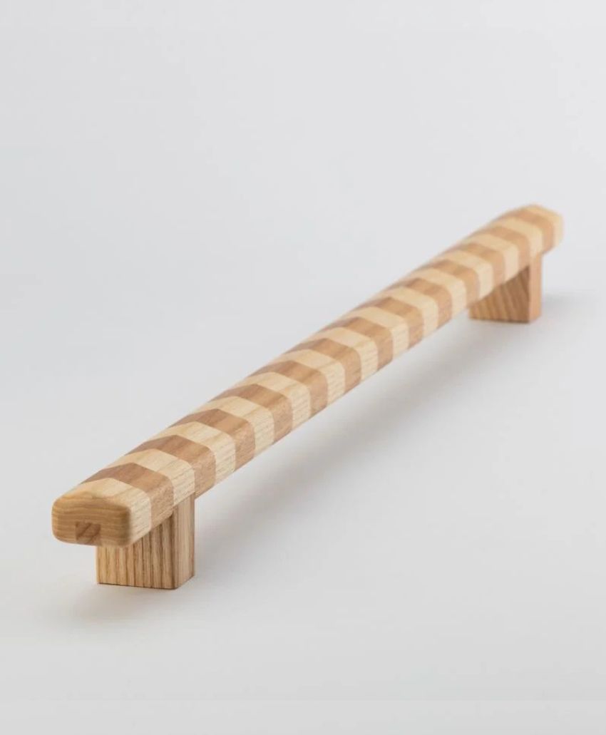 A wooden handle with alternating light and dark rectangular segments, supported by two block-shaped end pieces, set against a plain white background.