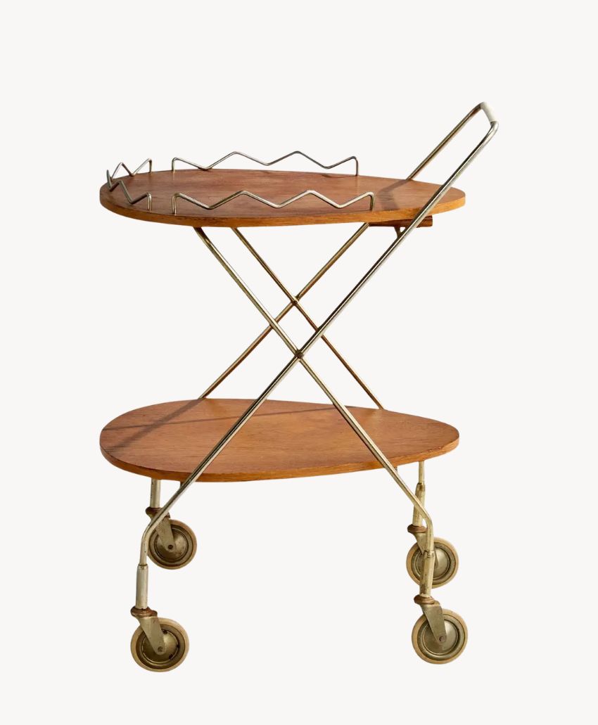 A vintage wooden bar cart with two oval shelves, metal frame, and four caster wheels. The top shelf has a metal rail, and the frame forms an X-shape on the sides.