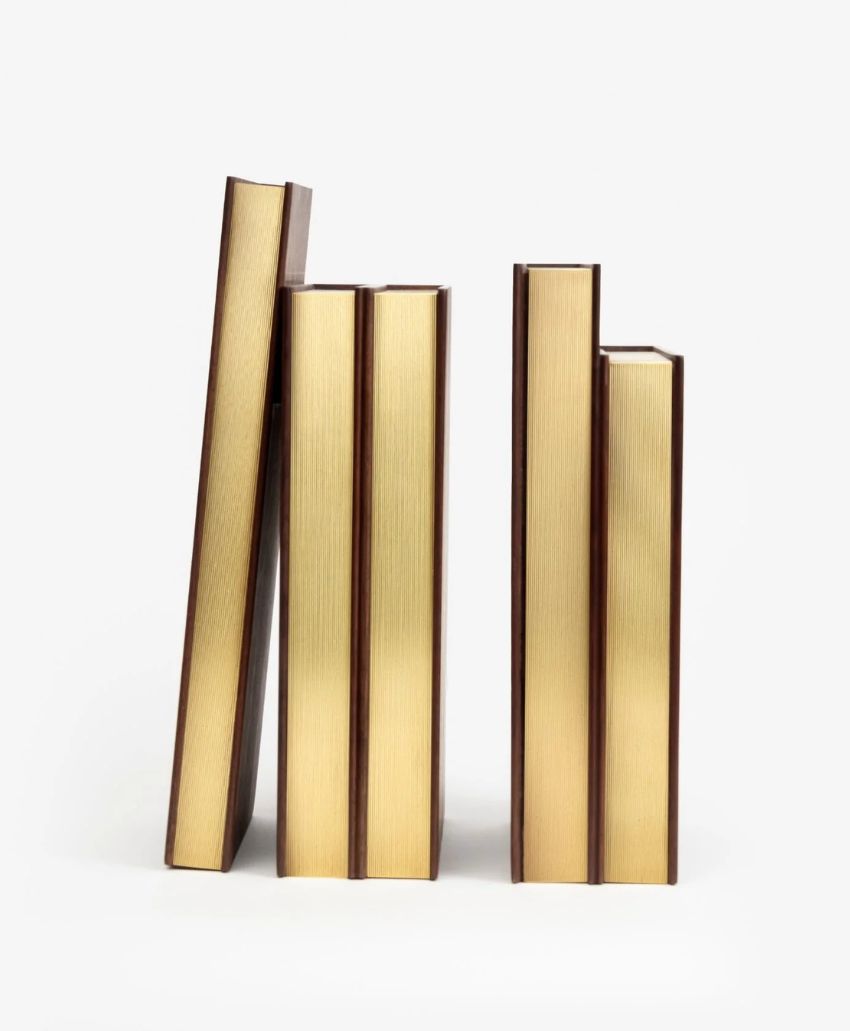Four gold-colored books stand upright and one leans to the left, all arranged in a row against a plain white background.