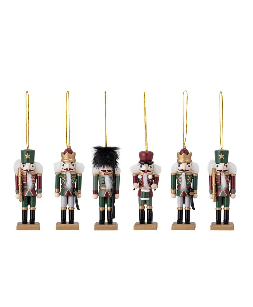 Six wooden nutcracker soldier ornaments, each with different hats and uniforms in green, red, and white, stand in a row with gold hanging loops attached to their heads.