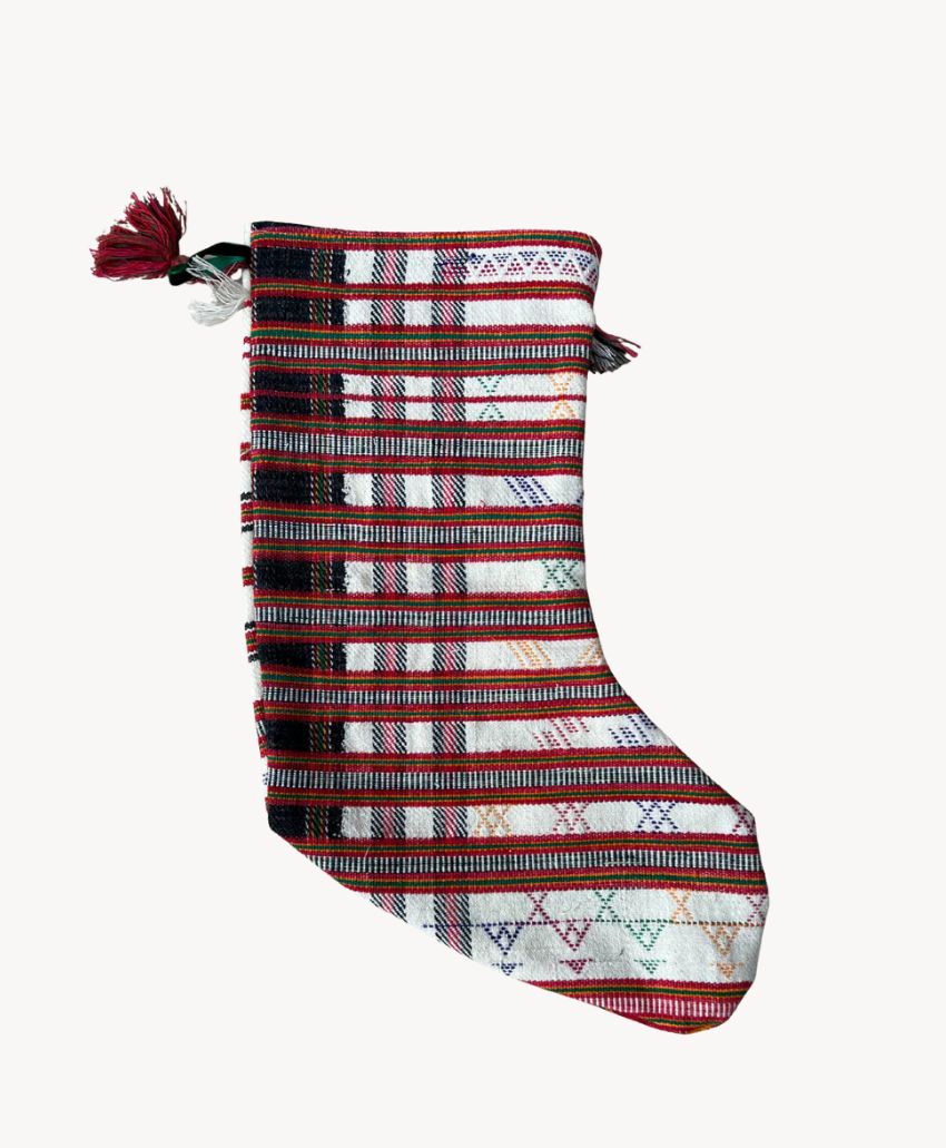 A Christmas stocking made of woven fabric with red, white, and brown horizontal and vertical stripes, featuring small decorative patterns and a tassel on the top left corner.