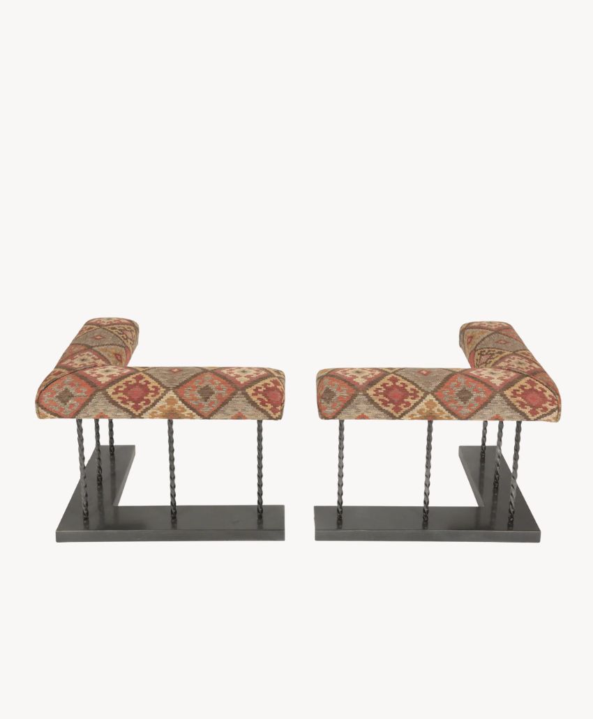 A pair of benches with upholstered seats featuring a red and beige geometric pattern, supported by metal rods and black rectangular bases, set against a plain white background.