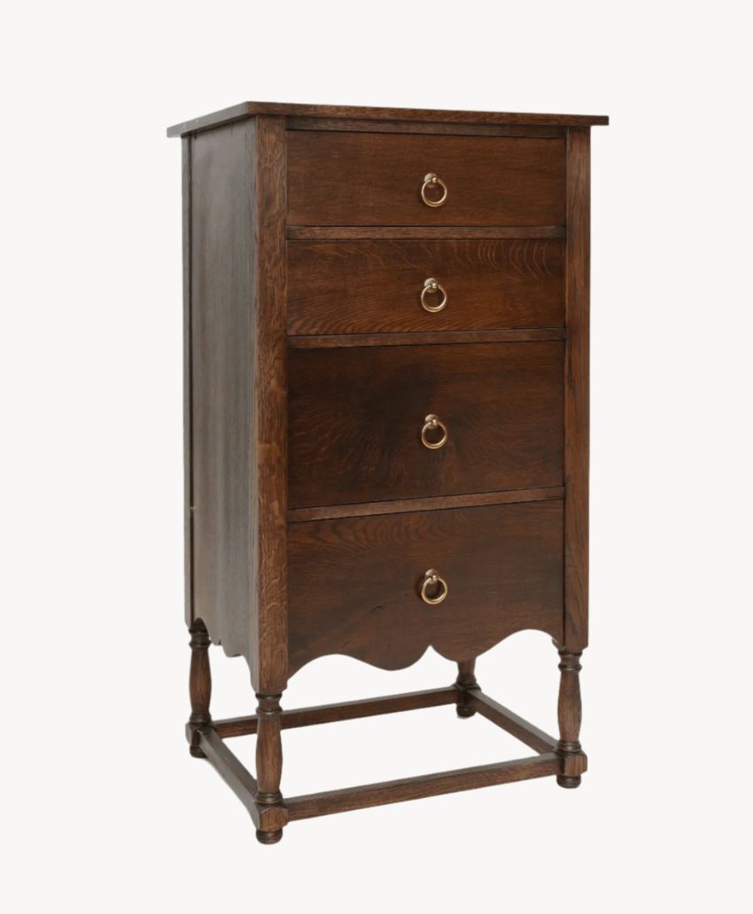 A tall, vintage wooden chest of four drawers with brass ring handles and decorative carved legs, standing on a light background.