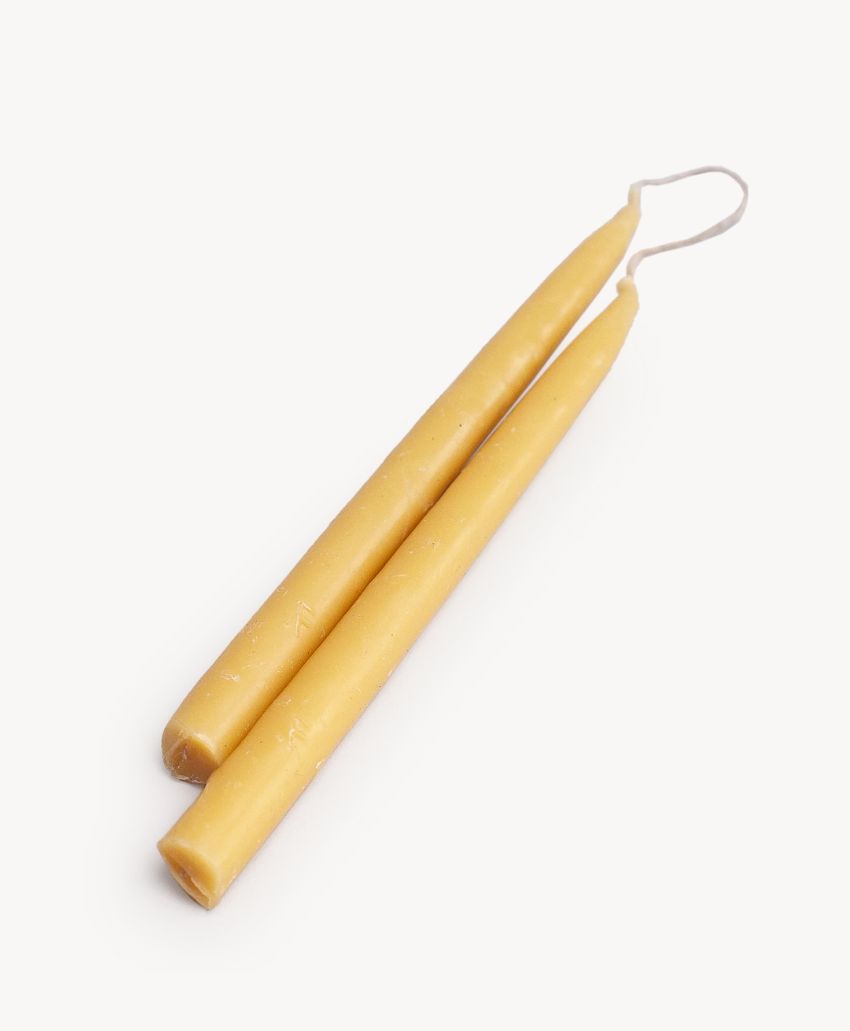 Two yellow taper candles joined at the top by a piece of wick, lying on a white surface.