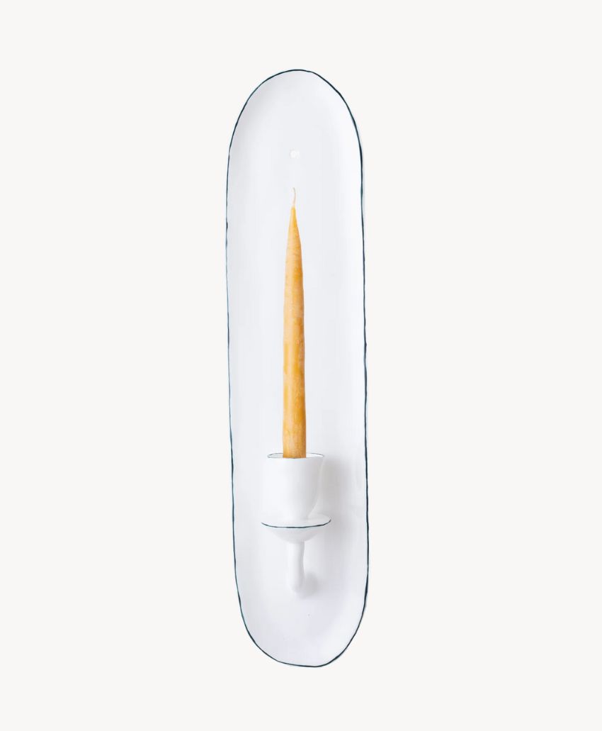 A white ceramic wall-mounted candle holder with a slim, upright taper candle, displayed against a plain white background.