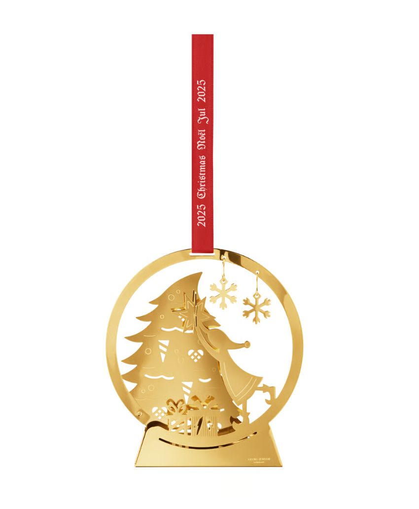 A gold Christmas ornament features a girl decorating a Christmas tree with stars, hanging from a red ribbon that reads “2025 Christmas Dec. 25, 2025” in white text.