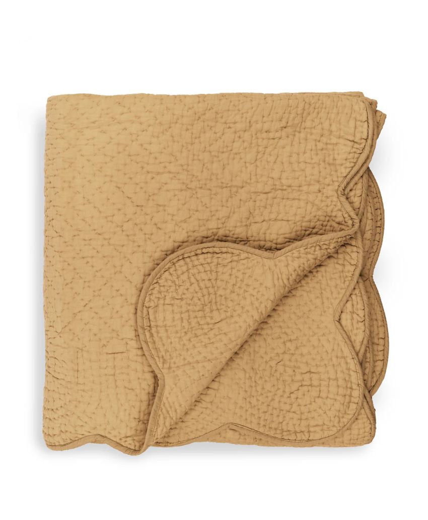 A folded tan quilt with a textured pattern and scalloped edges, neatly arranged so the decorative border is prominently visible.