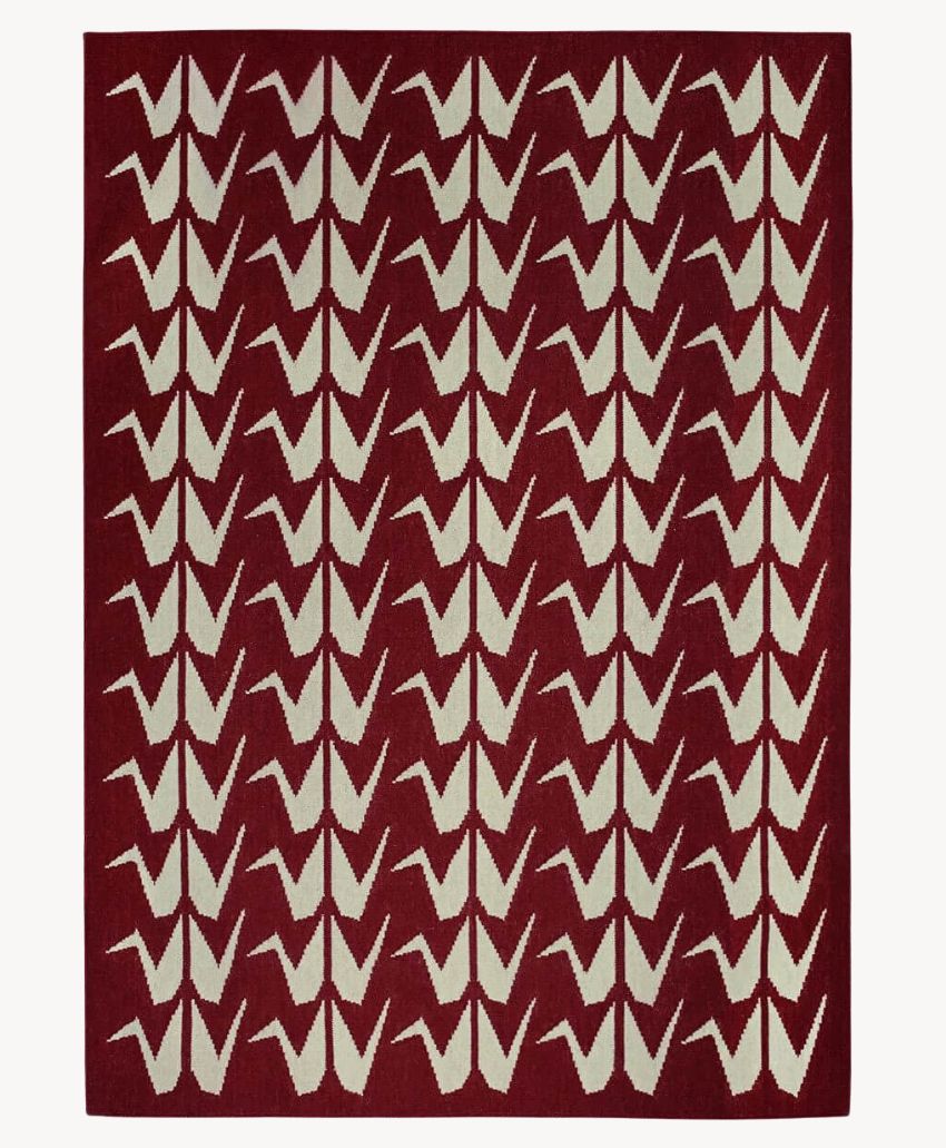 A rectangular rug with a deep red background featuring a repeating pattern of white origami cranes arranged in neat rows.