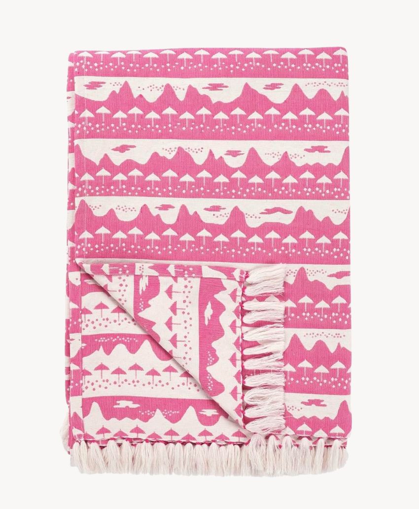 A folded pink and white blanket with a geometric and nature-inspired pattern, featuring fringed edges.