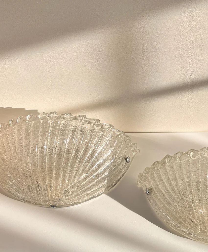 Two clear, textured glass bowls with scalloped edges rest on a white surface. Sunlight casts soft shadows and highlights the intricate patterns on the bowls and the wall behind them.
