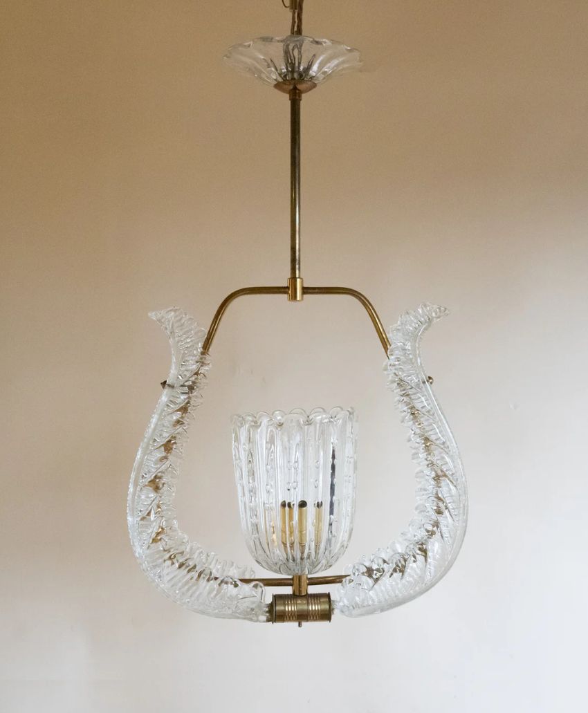 A vintage glass chandelier with a gold metal frame, featuring two curved textured glass arms and a ribbed glass central shade, hanging from a ceiling against a plain beige wall.