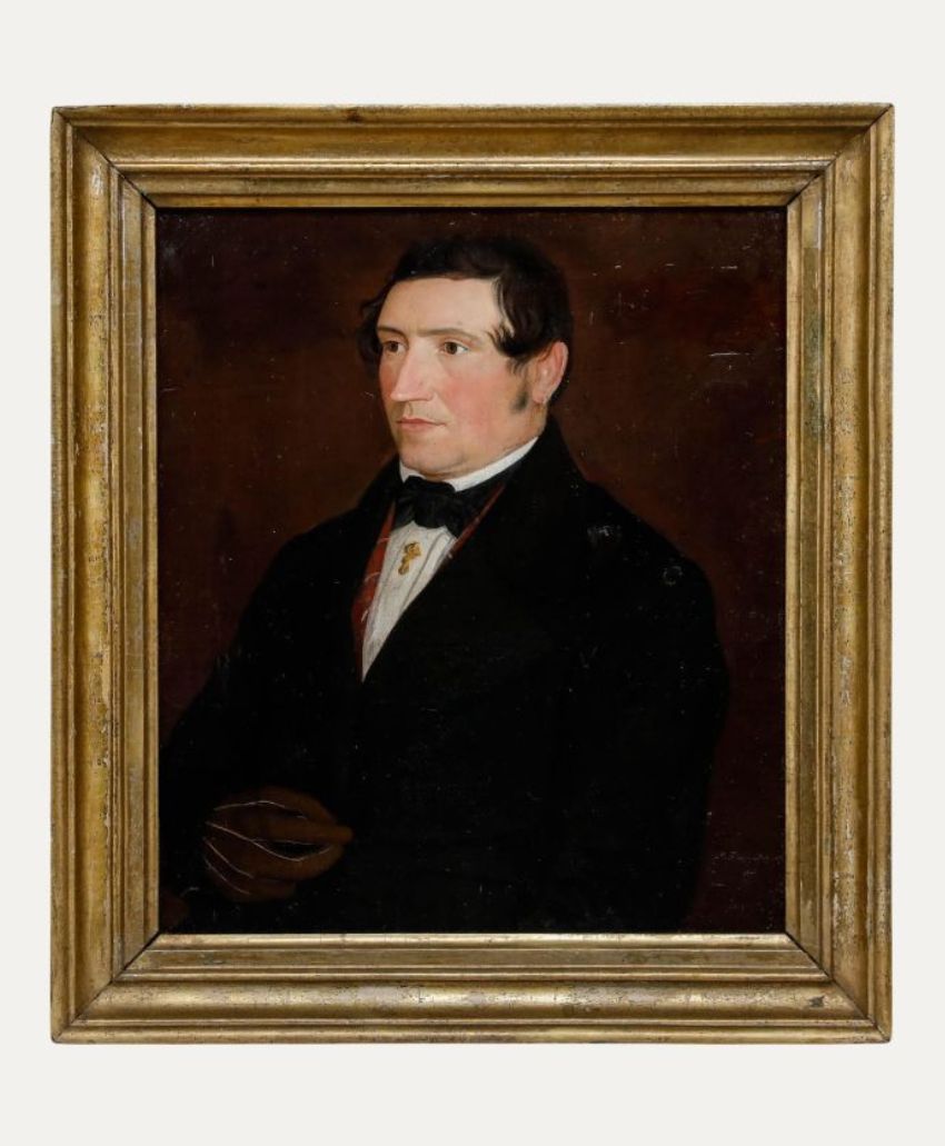 A framed oil painting of a man in dark formal clothing with a white shirt, dark jacket, and bow tie, set against a plain dark background. The man has short dark hair and is shown from the waist up, facing left.