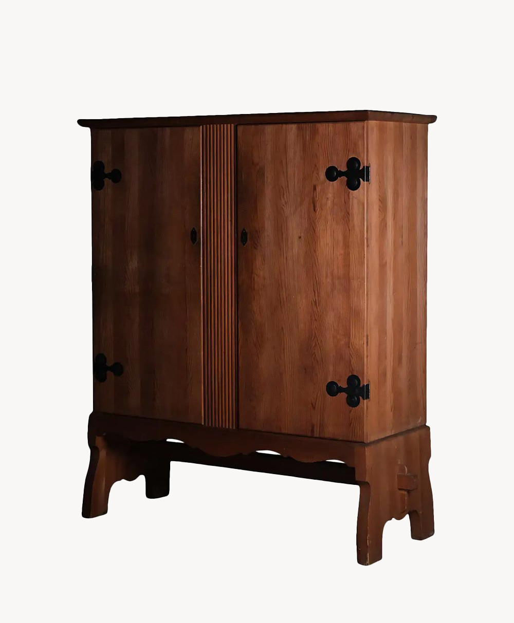 A wooden cabinet with two doors, decorative black metal hinges, and a grooved central design, standing on a sturdy, carved base.