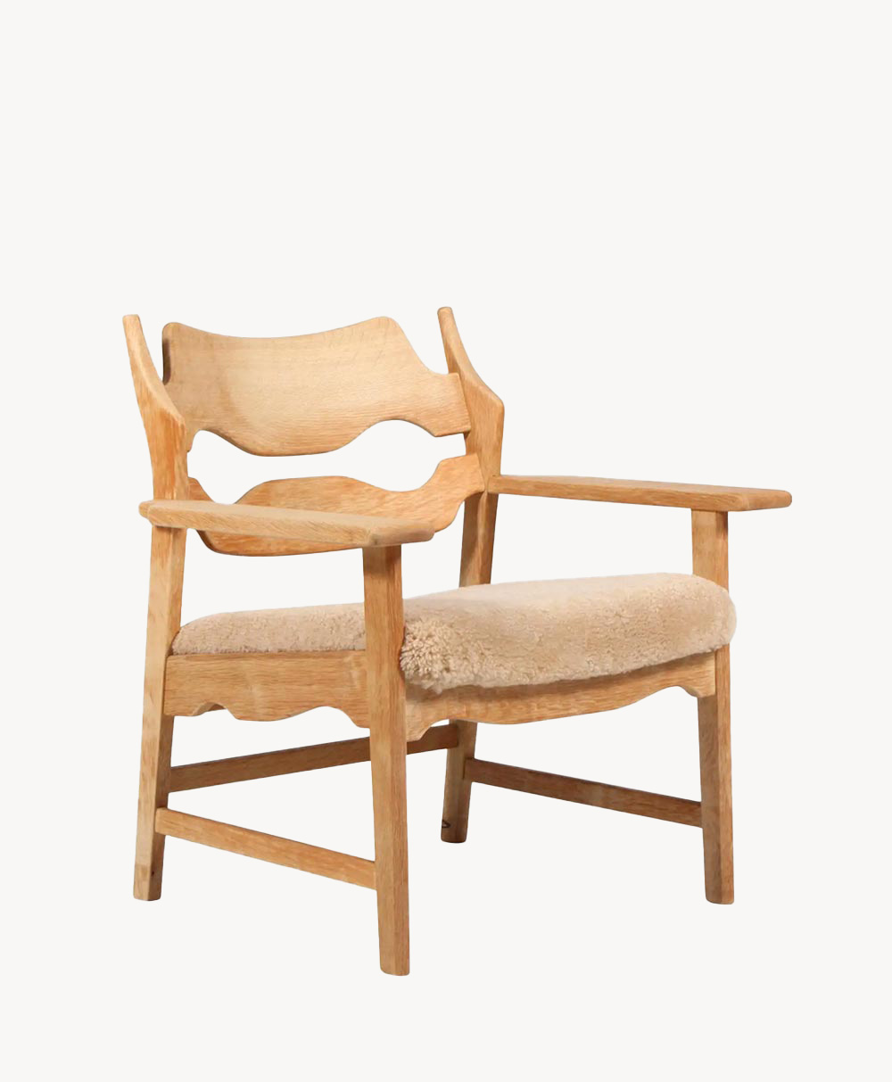A wooden armchair with curved armrests and backrest, featuring a light wood finish and a plush, beige upholstered seat cushion.