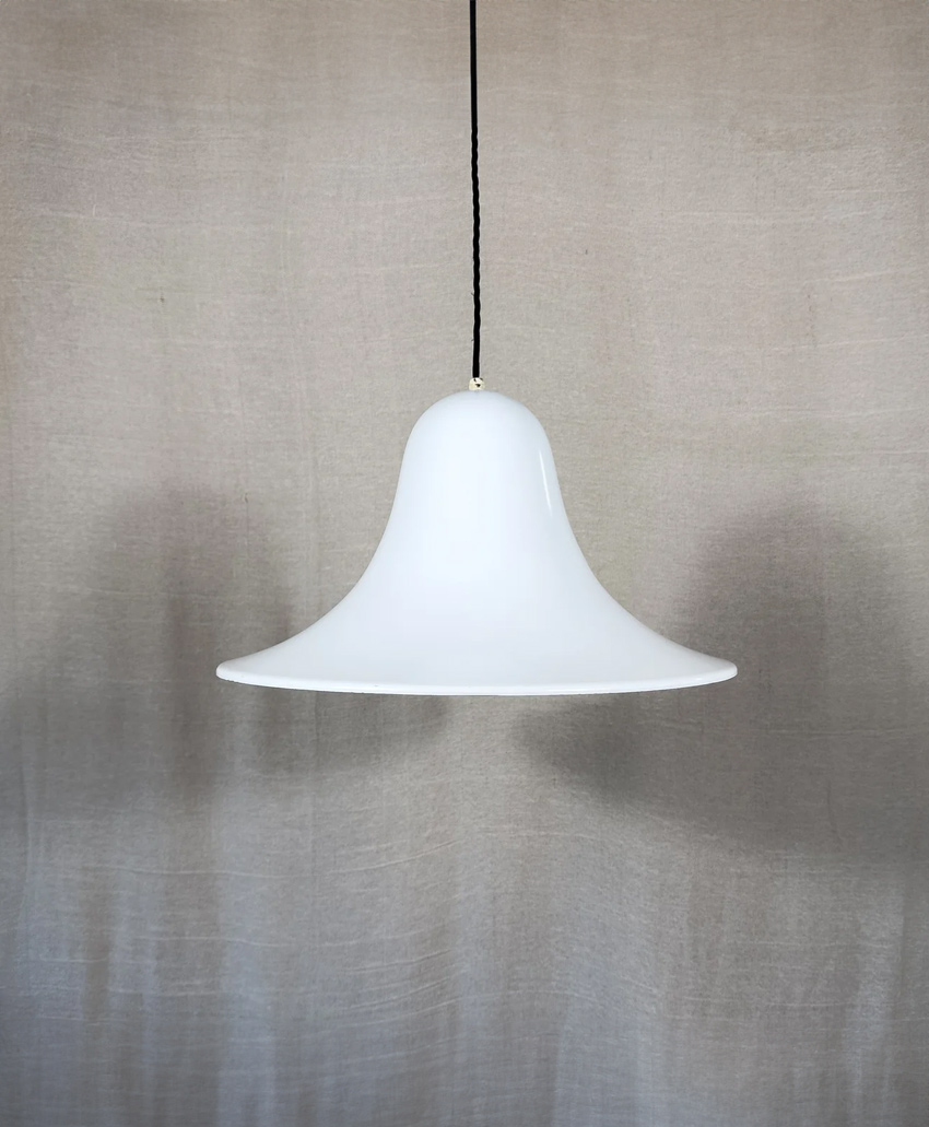 A white, bell-shaped pendant lamp with a smooth surface hangs from a black cord against a neutral, textured background.