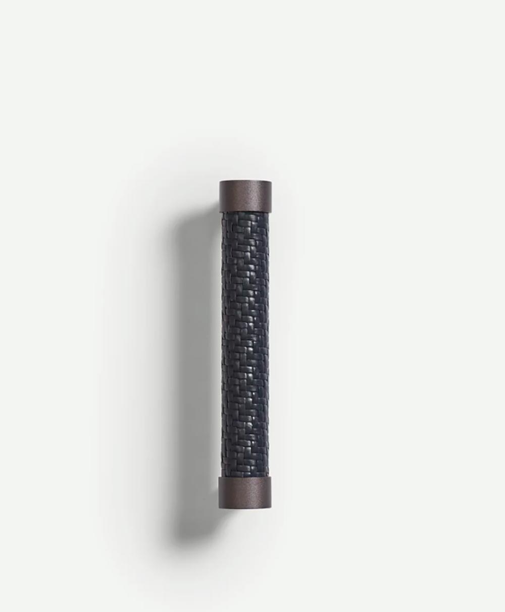 A cylindrical drawer or cabinet pull handle with a textured, woven dark center and smooth, metallic end caps, mounted vertically against a plain white background.