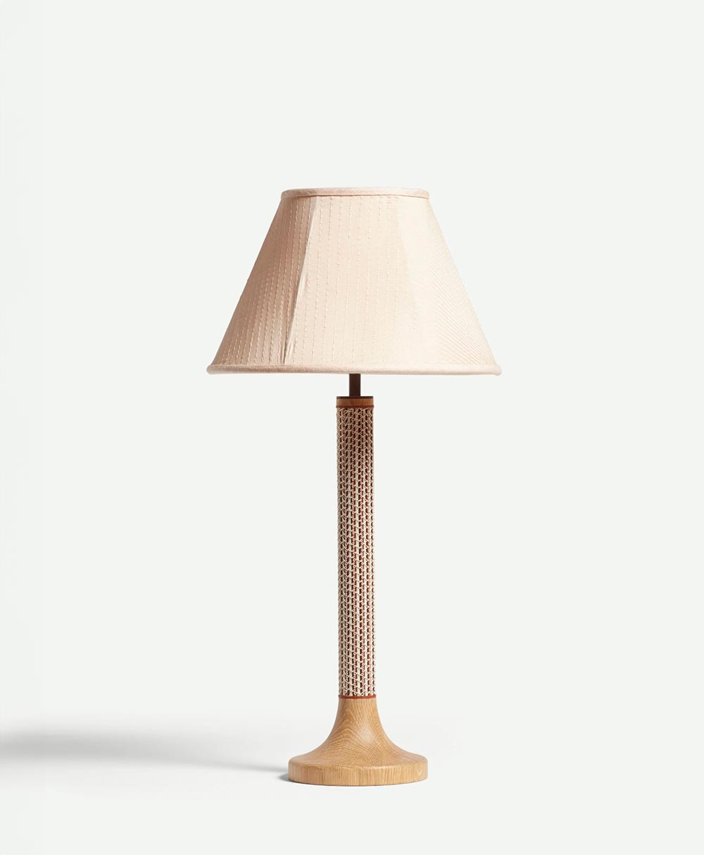 A table lamp with a beige fabric lampshade and a slender, textured stem on a round, light wood base, standing against a plain white background.