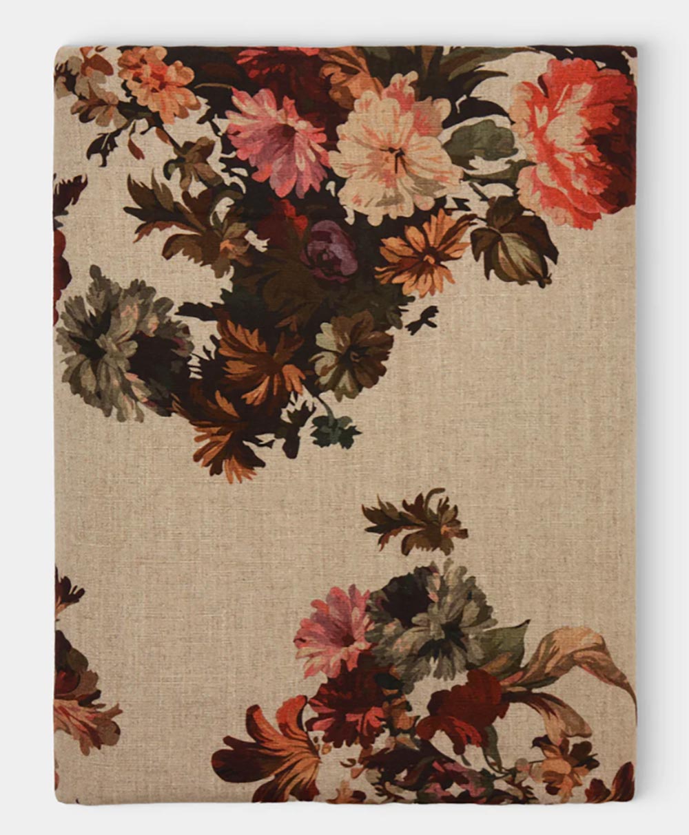 A beige fabric with clusters of colorful, vintage-style flowers in shades of red, pink, orange, and green scattered across the surface.