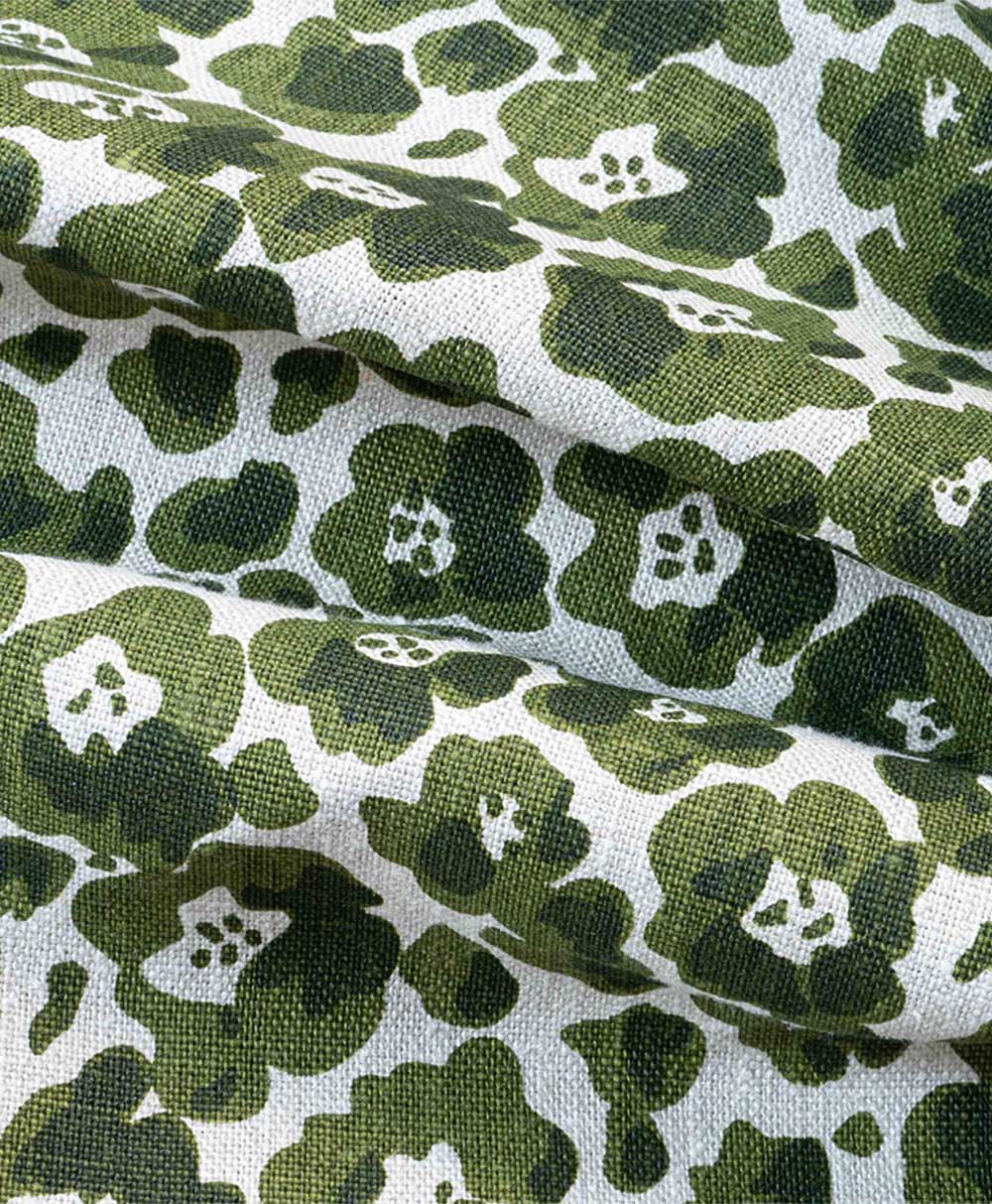 Green and white fabric with a floral print, featuring stylized green flowers and white centers on a textured surface. The fabric appears to have soft folds and a slightly rough texture.
