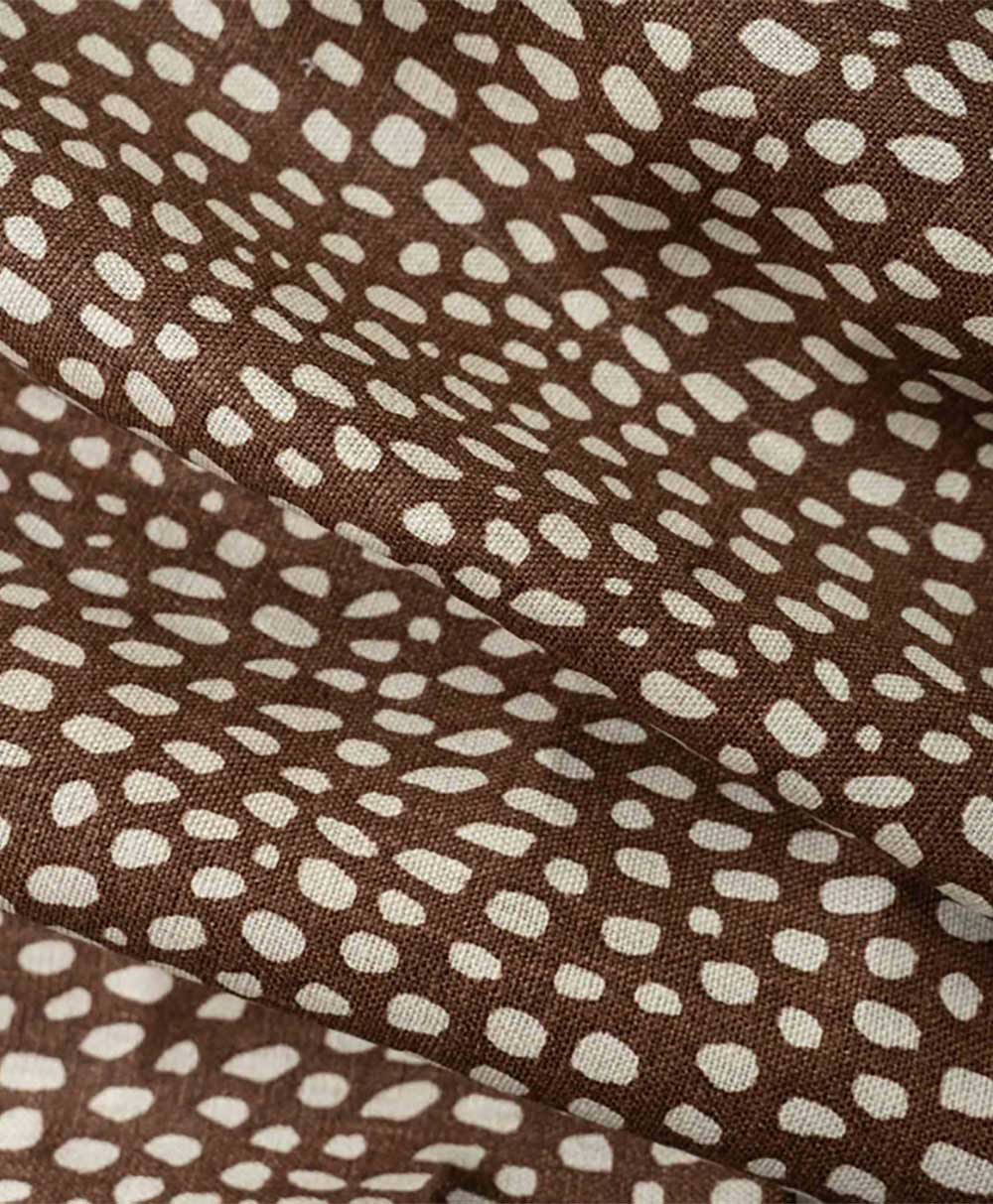 Brown fabric with a scattered pattern of irregular white dots, creating an abstract, organic, and slightly textured appearance. The fabric appears to have slight folds and creases.