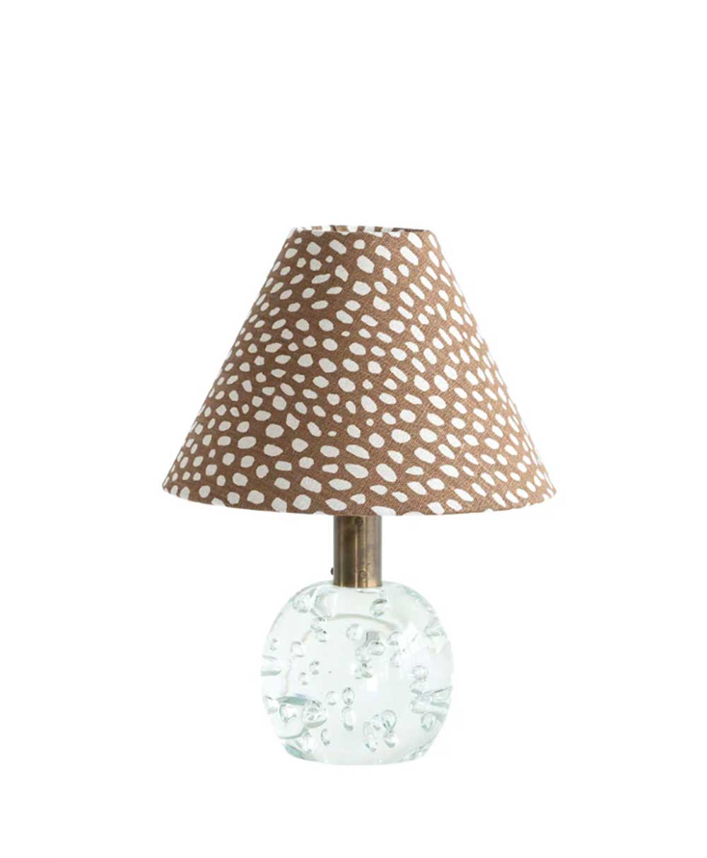 A table lamp with a round, clear glass base and a conical brown lampshade decorated with a white dotted pattern.