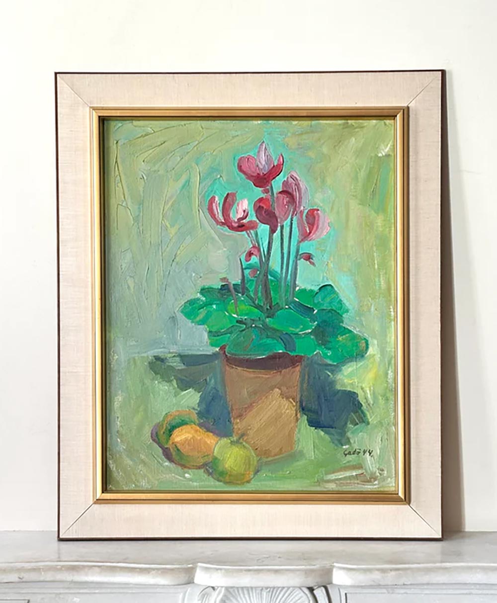 Framed painting of a potted plant with pink flowers and green leaves, set against a light green background, with two yellow fruits resting beside the pot. The artwork is displayed on a white surface.