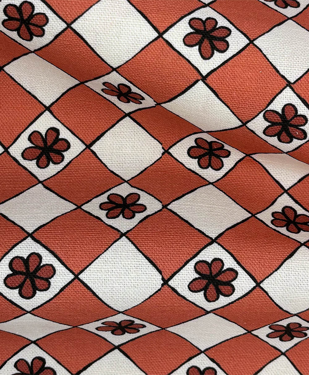 A patterned fabric with a red and white diamond grid design, each diamond containing a simple black flower with six petals. The fabric is slightly wrinkled.