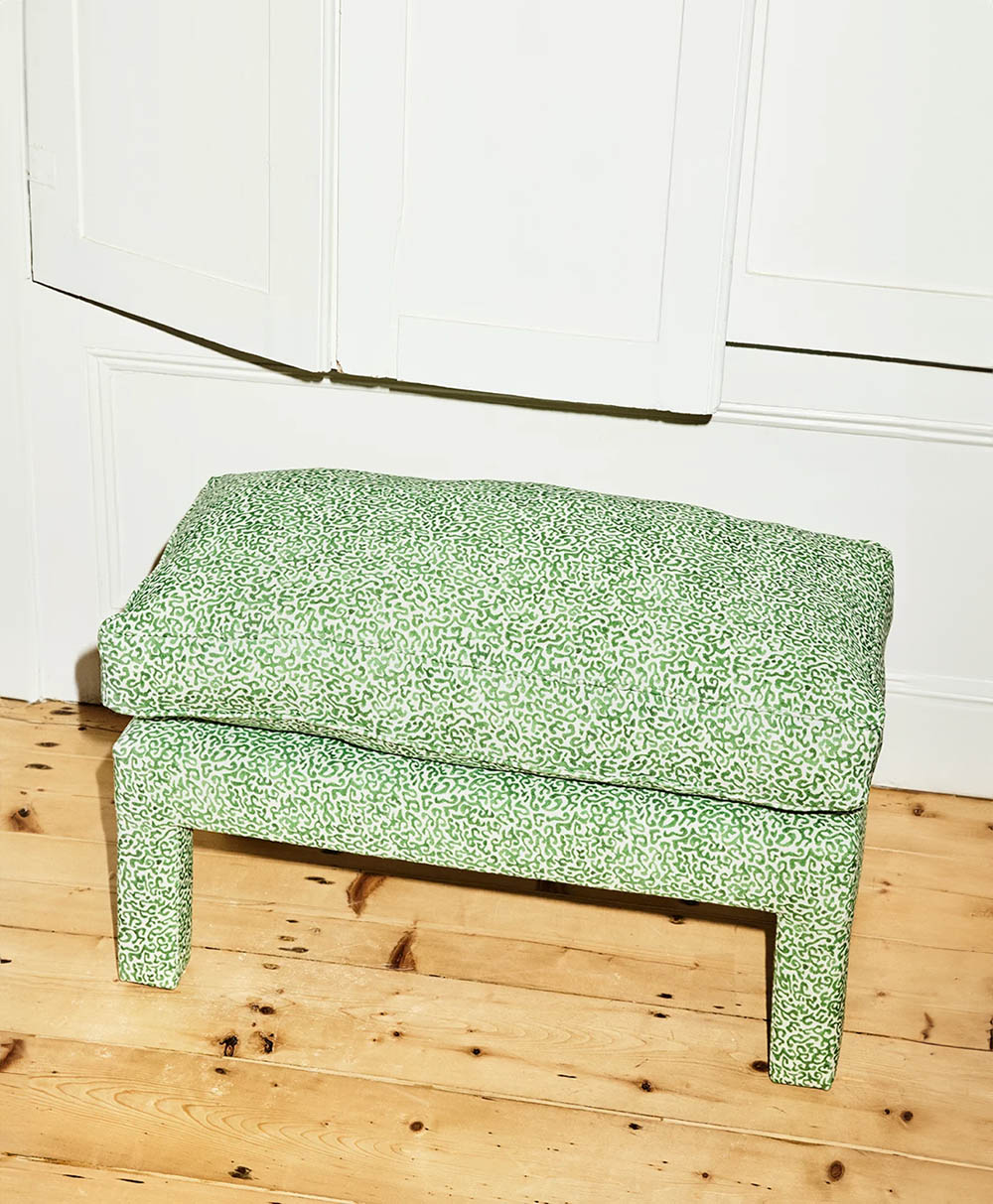 Green, patterned upholstered bench with a matching cushion, placed on a light wooden floor near a white wall and panel door.