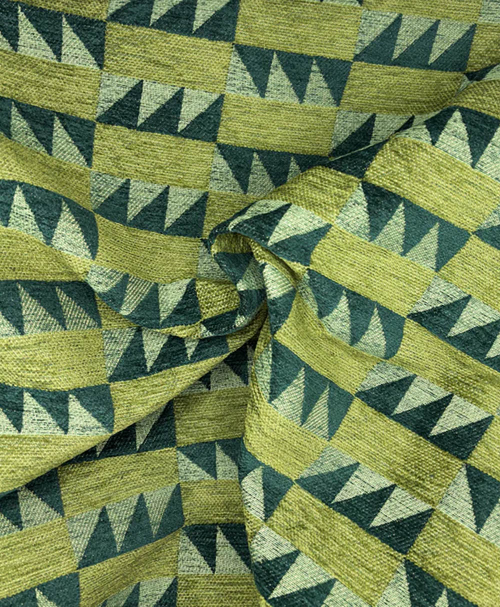 Green and yellow fabric with a geometric pattern of alternating triangles and rectangles, creating a visually dynamic, repeating design. The fabric is slightly wrinkled and gathered in the center.