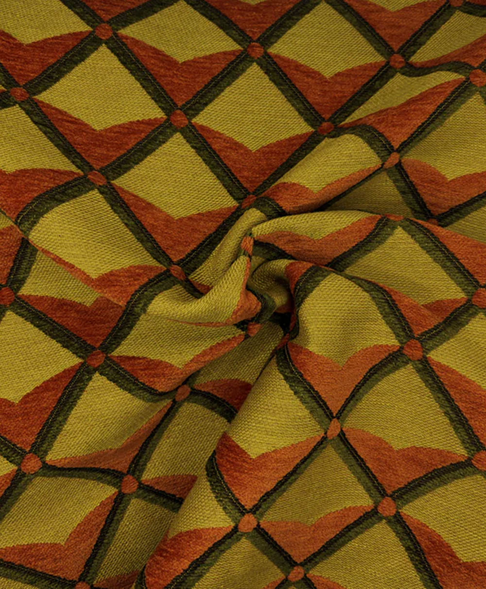 A close-up of fabric with a geometric pattern featuring olive green and rust orange shapes arranged in a diamond grid, intersected by dark lines, and slightly gathered at the center.