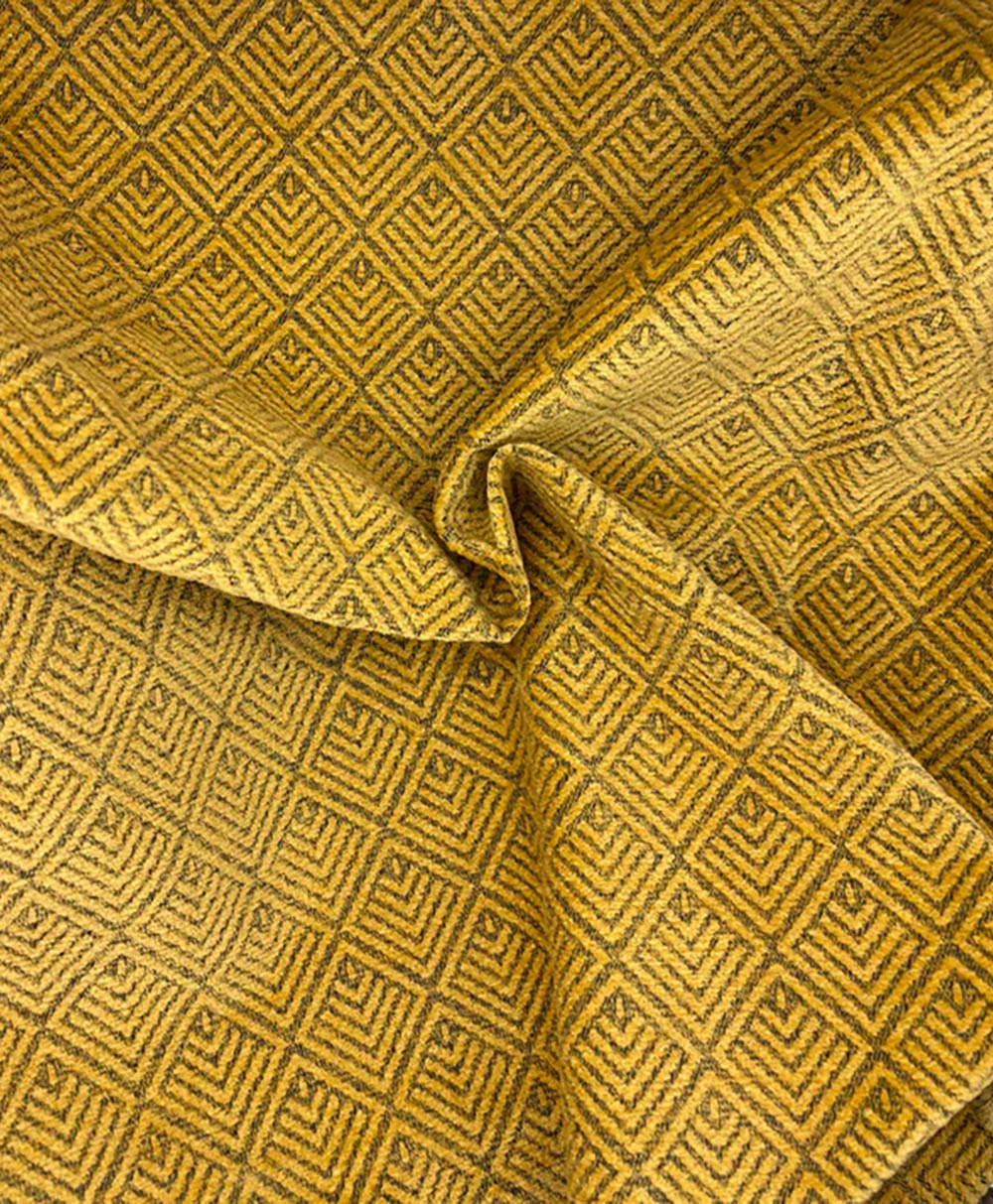 A close-up of yellow fabric with a geometric diamond pattern in dark brown, featuring folds and a slight twist in the center.