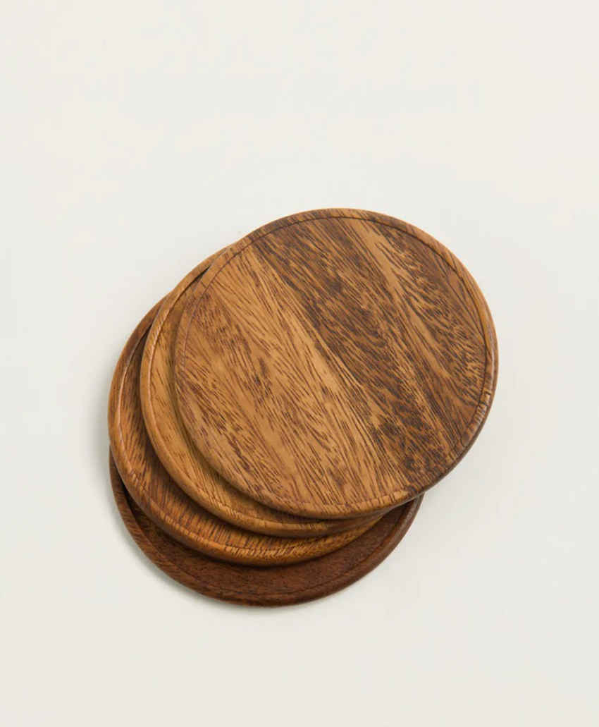 Three round wooden coasters with a natural grain pattern, stacked slightly askew on a plain, light-colored surface.