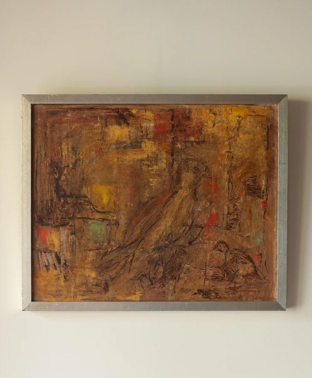 A framed abstract painting with earthy tones, featuring subtle shapes and brushstrokes that suggest the outline of a bird among textured, warm brown, yellow, and red areas. The artwork hangs on a plain light-colored wall.