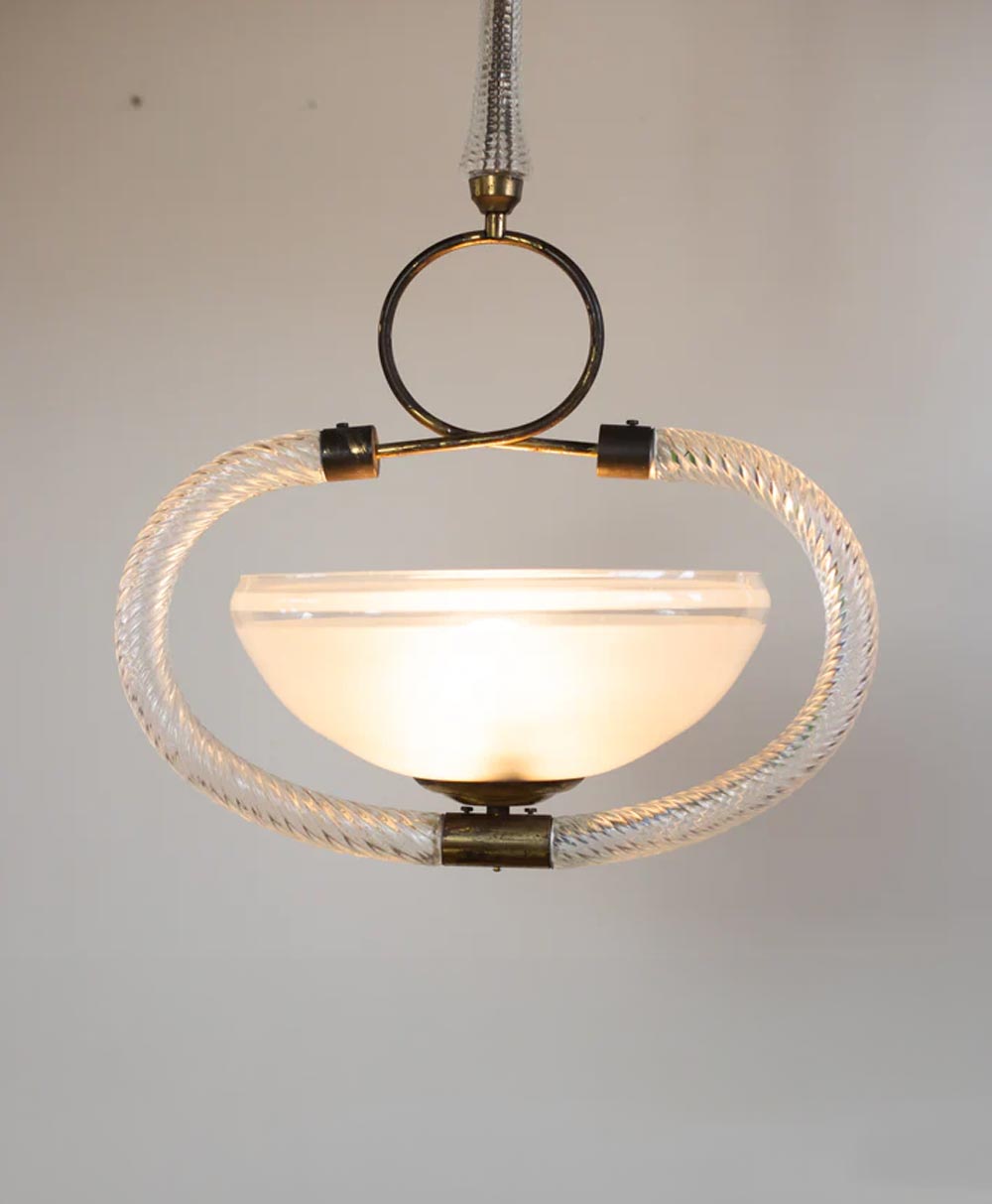 A vintage-style pendant light with a frosted glass bowl shade, brass fittings, and a decorative clear braided loop encircling the fixture, hanging against a plain background.