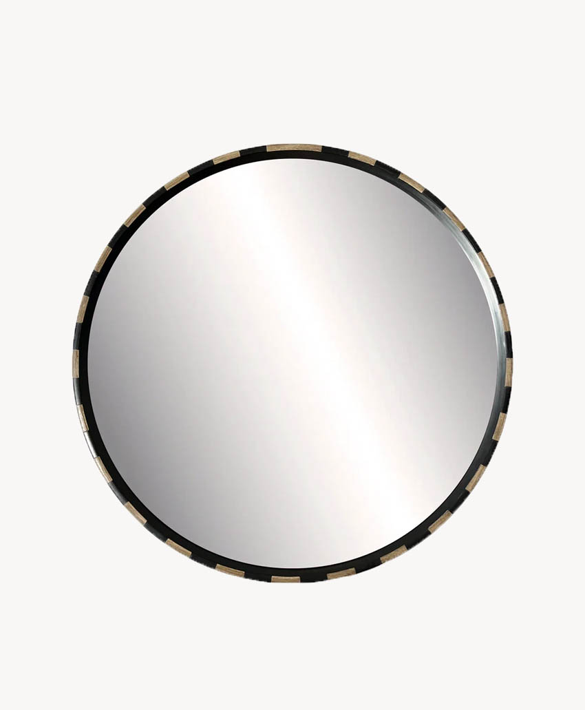 A round wall mirror with a black and gold segmented frame, reflecting light on its surface, set against a plain white background.