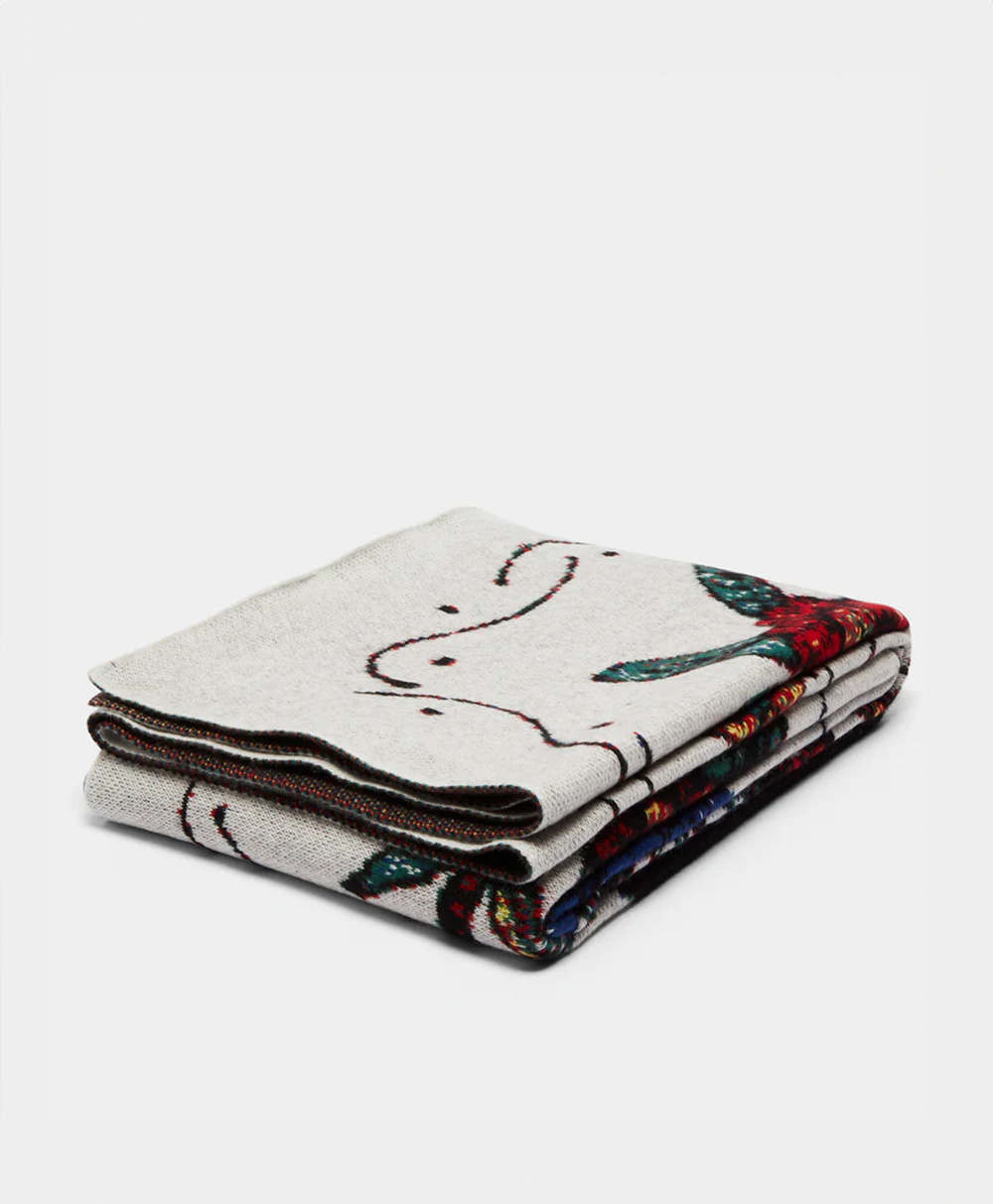 A light gray folded blanket with colorful abstract line and shape patterns, featuring hints of red, teal, and dark blue on the visible edges, placed on a plain white background.