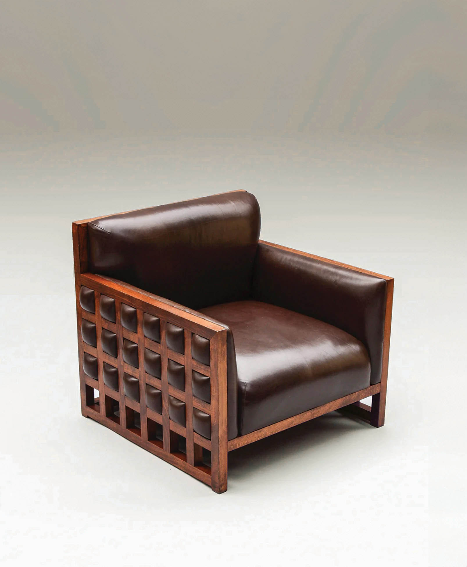 A modern armchair with dark brown leather cushions and wooden frame featuring a square grid pattern on the sides, set against a plain, light gradient background.